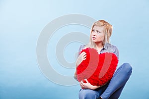 Sad woman holding red pillow in heart shape