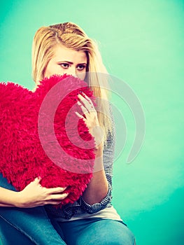 Sad woman holding red pillow in heart shape