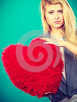 Sad woman holding red pillow in heart shape