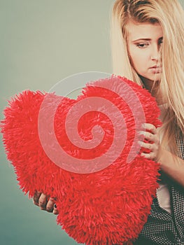 Sad woman holding red pillow in heart shape