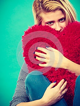 Sad woman holding red pillow in heart shape