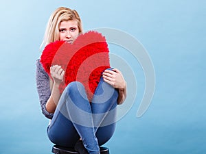 Sad woman holding red pillow in heart shape