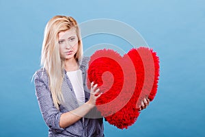 Sad woman holding red pillow in heart shape