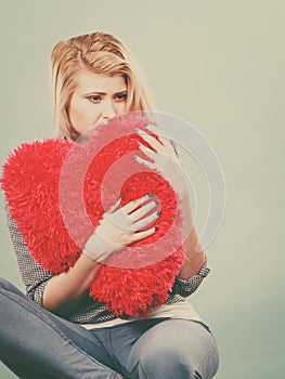 Sad woman holding red pillow in heart shape