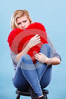 Sad woman holding red pillow in heart shape