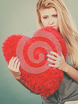 Sad woman holding red pillow in heart shape