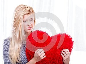 Sad woman holding red pillow in heart shape