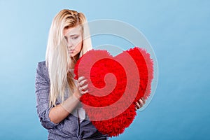 Sad woman holding red pillow in heart shape