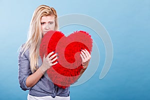 Sad woman holding red pillow in heart shape