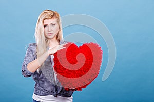 Sad woman holding red pillow in heart shape