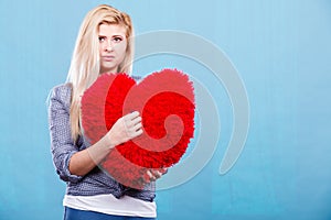 Sad woman holding red pillow in heart shape