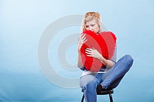 Sad woman holding red pillow in heart shape