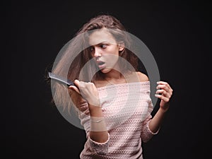 Sad woman holding tangled hair on the black background. Tuft of hair on a girl`s hand. Hair loss concept. Copy space.