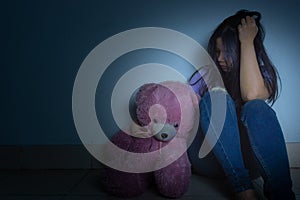 sad woman hug her knee and cry sitting with teddy bear in a dark room. Depression, unhappy, stressed and anxiety disorder concept