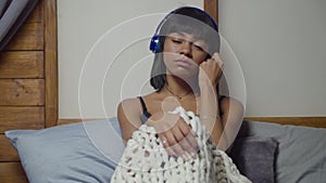 Sad woman listening music with earphones on bed