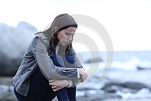 Sad woman looking down sitting alone on the beach