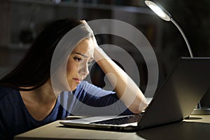 Sad woman looking at laptop at night at home