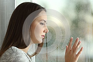 Sad woman looking rain through a window