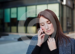 Sad woman looks at floor and talking on a phone in city downtown. Business woman stress concept