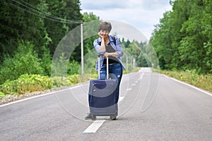 Sad woman with a luggage standing in the middle of a asphalt road and waiting for help