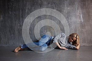 Sad woman lying on the floor. Depression and chronic fatigue. Young beautiful blonde in a gray sweater and jeans