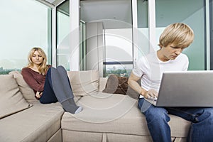 Sad woman beside man using laptop in living room at home