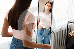 Sad Woman Measuring Waist After Weight Gain Standing At Home