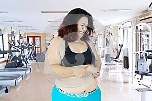 Sad woman pinching her belly fat in gym center