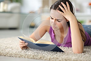 Sad woman reading a paper book on a carpet at home