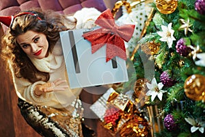 Sad woman with scale and bow near Christmas tree and gift boxes