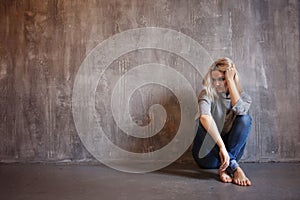 Sad woman sits on the floor. Depression and chronic fatigue. Young beautiful blonde in a gray sweater and jeans