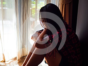 Sad woman sitting alone in a empty room beside window or door