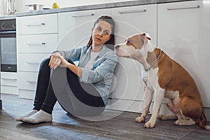 Sad woman sitting on a kitchen floor with her dog