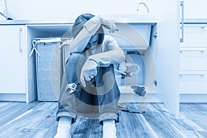 Sad woman sitting near leaking sink in laundry room holding adjustable wrench