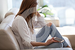 Sad woman sitting on sofa holding phone waiting for call