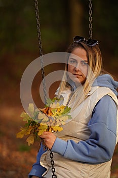 Sad woman sitting on a swing and holding a bouquet of wildflowers