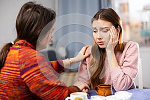 Sad woman sitting at table with her friend who supporting her