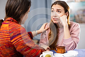 Sad woman sitting at table with her friend who supporting her