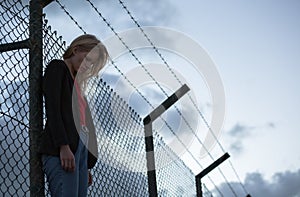 Sad woman standing alone against barbed wire fence