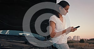 Sad woman standing front to broken car and using smartphone to find service