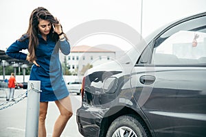 Sad woman standing near car with scratch