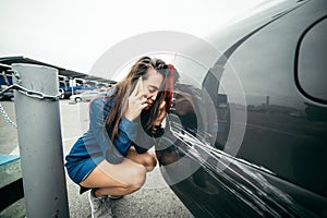 Sad woman standing near car with scratch
