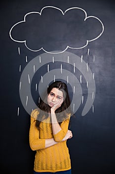 Sad woman standing under raincloud drawn above her on blackboard