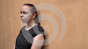 Sad woman stands near wall and gets wet in rain. Drenched female under downpour on street in summertime.