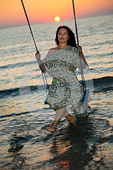 Sad woman in swing against sea at sunrise