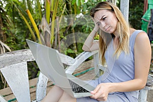 Sad woman using laptop and sitting in exotic garedn with palms in background.