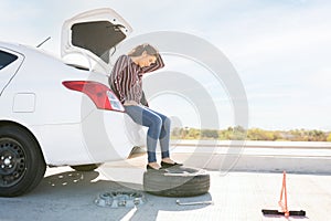Sad woman waiting for help to change her car flat tire