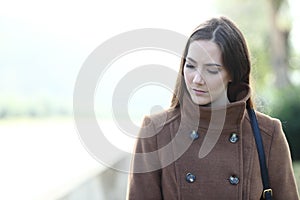 Sad woman walking alone in a park looking down