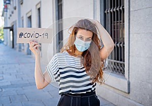 Sad woman wearing face mask outdoors holding COVID-19 sign. Coronavirus Health crisis concept