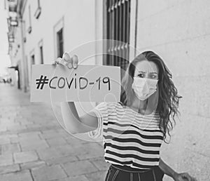 Sad woman wearing face mask outdoors holding COVID-19 sign. Coronavirus Health crisis concept